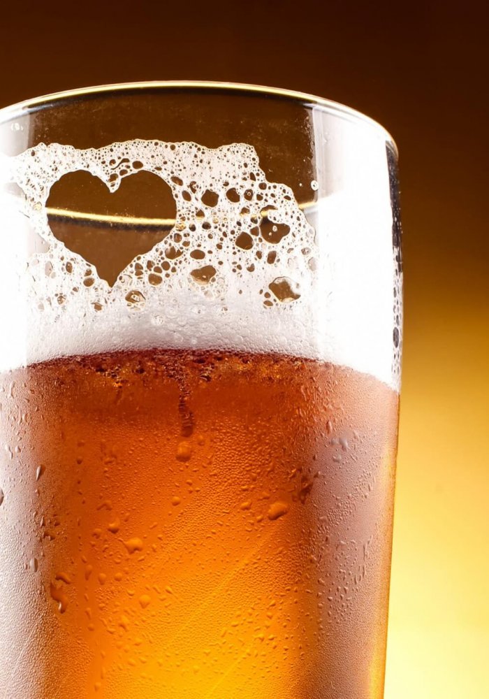 Glass of beer with the heart represented with froth close up over yellow background